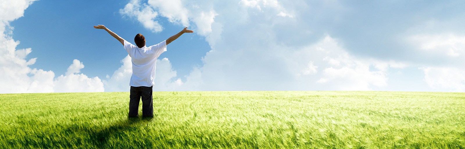 man standing in a field arms stretched to the sky